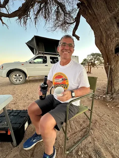 Happy client sitting in a camp chair next to a Namib Trails 4x4 with rooftop tent