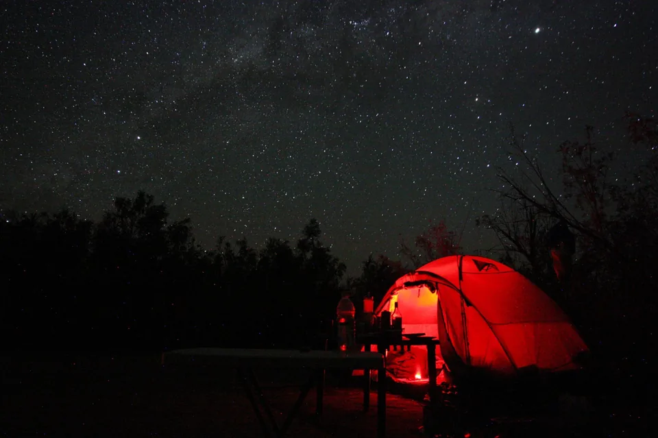 Red-lit camping tent under a star-filled Namibian night sky
